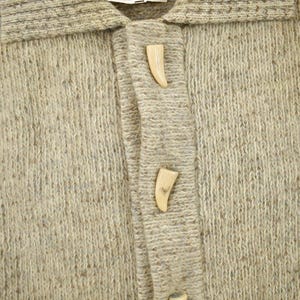 May include: Close-up of a light brown cardigan sweater with a collar and two decorative horn-shaped buttons. The sweater is made of a textured knit fabric.