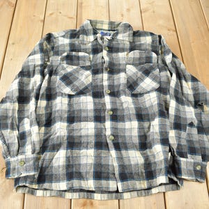 May include: A long-sleeved flannel shirt with a black and white plaid pattern. The shirt has a button-up front and two chest pockets.