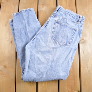 Puede incluir: Un par de pantalones vaqueros de mezclilla azul claro doblados por la mitad, sobre una superficie de madera.