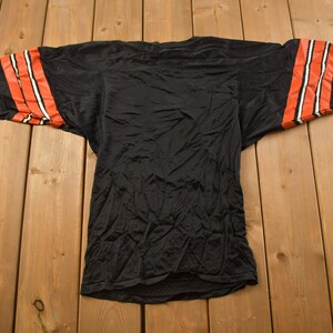Op de afbeelding: Zwart shirt met oranje en witte strepen op de mouwen. Het shirt is gemaakt van mesh-materiaal en heeft een losse pasvorm.