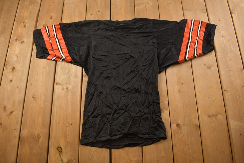 Op de afbeelding: Zwart shirt met oranje en witte strepen op de mouwen. Het shirt is gemaakt van mesh-materiaal en heeft een losse pasvorm.