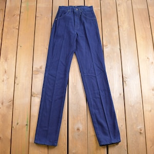 May include: A pair of dark blue denim jeans laid flat on a wooden surface.
