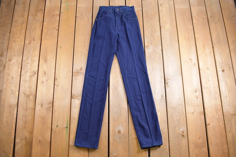 May include: A pair of dark blue denim jeans laid flat on a wooden surface.