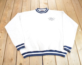 May include: White sweatshirt with a navy blue ribbed crew neck and cuffs. The sweatshirt has a navy blue embroidered logo that reads "Memorial Golf Classic Kari St. Well Tournament 1993".