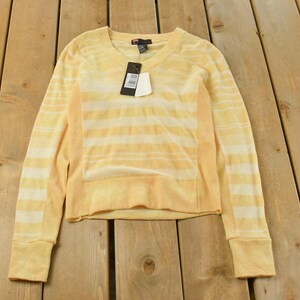 May include: A yellow and white striped sweater with long sleeves and a crew neck. The sweater has a tag attached. The garment is displayed on a wooden surface.