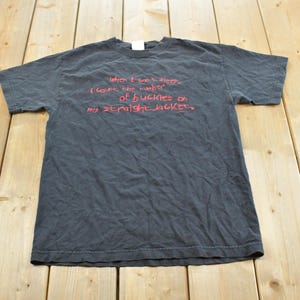May include: A black short-sleeved t-shirt featuring red text printed on the chest that reads, "When I can't sleep, I count the number of buckles on my straightjacket." The shirt has a crew neckline and a standard fit with a plain back.