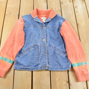 Puede incluir: Chaqueta vaquera vintage con mangas y cuello de punto color coral. La chaqueta tiene cierre de botones, dos bolsillos delanteros y un estampado de inspiración suroeste en los puños de las mangas. Una prenda de abrigo elegante.