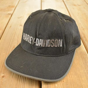 Puede incluir: Gorra de béisbol negra con el texto bordado "HARLEY-DAVIDSON" en plata. La gorra tiene una visera curva con un borde gris. El sombrero está hecho de una tela duradera.
