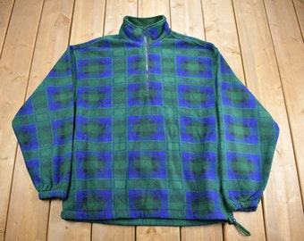 May include: A green and blue plaid fleece pullover with a quarter zip closure. The fleece has a soft, fuzzy texture.