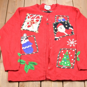 K&ouml;nnte beinhalten: Rote Strickjacke mit Weihnachtsmotiv. Sie zeigt gestickte Bilder von einer Katze, dem Weihnachtsmann, einem Zuckerstangen, einem Weihnachtsbaum und einer Stechpalme.