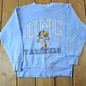 May include: A light blue sweatshirt with the text "UNC Tarheels" and a cartoon mascot in the center.