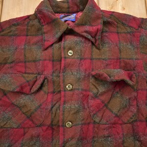 May include: A red and brown plaid flannel shirt with a button-up front and two flap pockets. The shirt is made of a soft, brushed fabric.