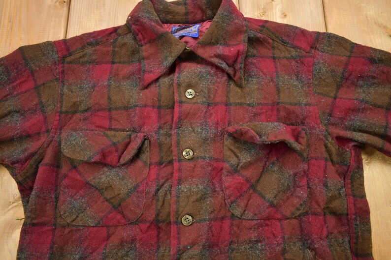 May include: A red and brown plaid flannel shirt with a button-up front and two flap pockets. The shirt is made of a soft, brushed fabric.