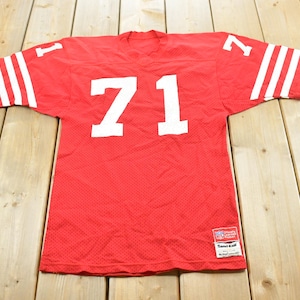 Könnte beinhalten: Ein rotes Football-Trikot aus Mesh mit der weißen Nummer 71 auf der Vorderseite und den Schultern. Die Ärmel haben drei weiße horizontale Streifen. Ein kleines NFL-Logo-Emblem und ein weißes rechteckiges Etikett sind unten vorne sichtbar.