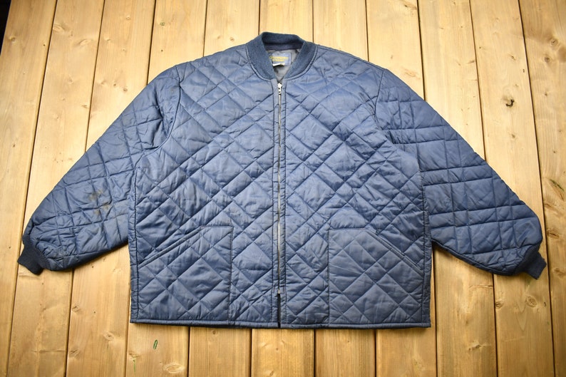 May include: A navy blue quilted jacket with a zipper closure and two pockets. The jacket has a diamond pattern and a ribbed knit collar and cuffs.