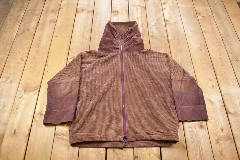 May include: A brown corduroy hooded jacket with a zipper closure. The jacket has a drawstring at the bottom and is made of a soft, comfortable fabric.