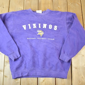 May include: Purple sweatshirt with the word "VIKINGS" in white letters and a purple and gold Viking helmet logo. The text "NATIONAL FOOTBALL LEAGUE" is printed below the logo.