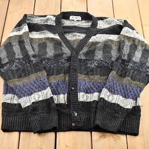 May include: A striped cardigan sweater with a V-neck and button closure. The sweater is made of a soft, knitted fabric and features a variety of colors, including black, gray, white, and purple.