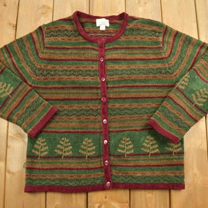 Könnte beinhalten: Ein grün-braun-burgunder gestreifter Cardigan mit Knopfleiste. Der Pullover hat ein Muster aus kleinen Bäumen an den Ärmeln und vorne.