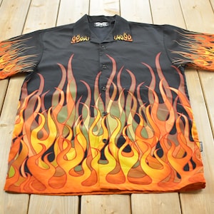 May include: A black short-sleeve button-down shirt featuring a vibrant flame pattern in shades of orange, yellow, and red. The design covers the front, sleeves, and collar, with a standard collar, a front button placket, and a straight hemline.