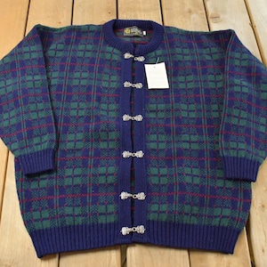 Peut inclure: Un cardigan en tricot à manches longues avec un motif à carreaux bleu foncé, vert et rouge. Le vêtement présente un col rond, des poignets et un ourlet côtelés bleu foncé. Il se ferme sur le devant par cinq fermoirs métalliques argentés.
