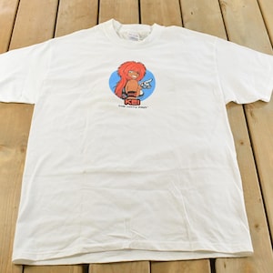 May include: White t-shirt featuring a cartoon graphic of a character with red hair, a blue circle background, and the text "KEI THE CURVY GIRL". The shirt is made of a soft, comfortable material.