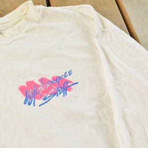 May include: Cream-colored long-sleeve t-shirt with a crew neck. The shirt features a graphic in pink and blue that reads "Motorcycle Staff". The shirt is made of a soft, lightweight material.