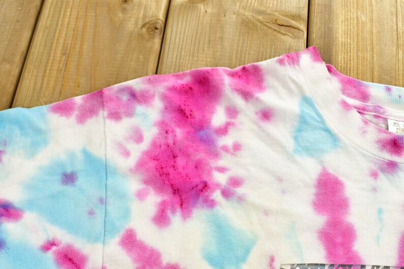 May include: A white t-shirt with a tie-dye pattern in shades of pink and blue.