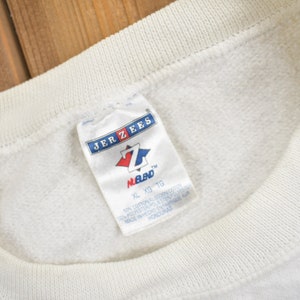K&ouml;nnte beinhalten: Wei&szlig;er Jerzees-Sweatshirt mit einem Etikett mit der Aufschrift "XL XG TG" und "M.B.D."