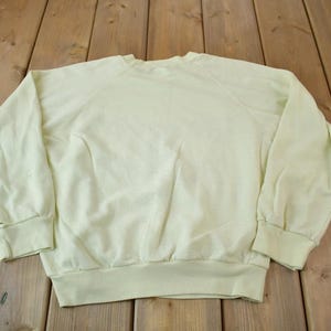 May include: A pale yellow sweatshirt with a crew neck and long sleeves. The sweatshirt is made of a soft, comfortable fabric.