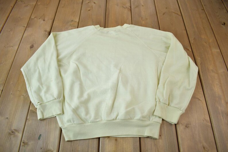 May include: A pale yellow sweatshirt with a crew neck and long sleeves. The sweatshirt is made of a soft, comfortable fabric.