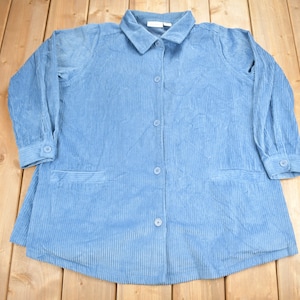 May include: A light blue corduroy shirt with a button-up front and long sleeves. The shirt has two pockets on the front.