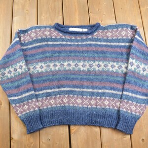 Könnte beinhalten: Ein gestrickter Pullover in Blau, Lila und Weiß mit einem Fair Isle Muster. Der Pullover hat einen Rundhalsausschnitt und lange Ärmel.