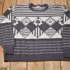May include: A gray and white patterned sweater with a crew neck. The sweater has a geometric design with diamonds and stripes.