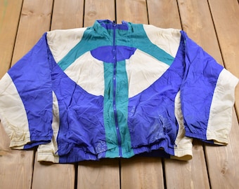 May include: A blue, white, and teal windbreaker jacket with a zipper closure. The jacket has a geometric pattern and a drawstring at the waist.