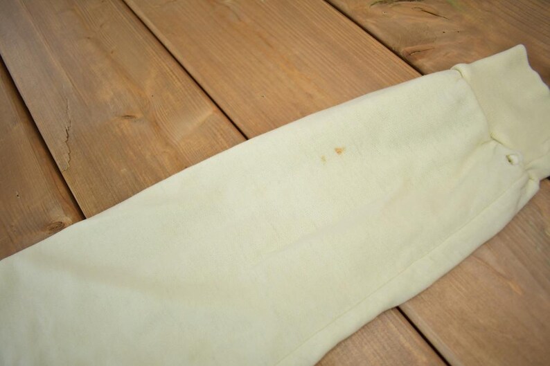 May include: A close-up of a light cream colored fabric with a small brown stain. The fabric is smooth and appears to be made of cotton.