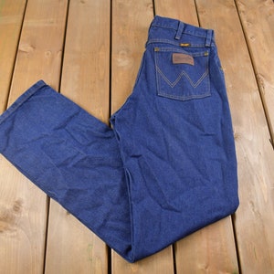 May include: A pair of dark blue denim jeans with a brown leather patch on the back pocket that says "Wrangler".