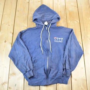 May include: A blue zip-up hoodie with a hood and white drawstrings. The hoodie has the text "USCG AUXILIARY" printed on the front, along with a small graphic of flags. The hoodie is made of a soft material.