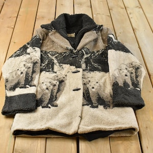 May include: A long-sleeved coat featuring a textured beige and black fleece fabric with a repeating graphic print of polar bears. The coat includes a dark charcoal gray collar, matching sleeve cuffs, and three black toggle closures down the front.