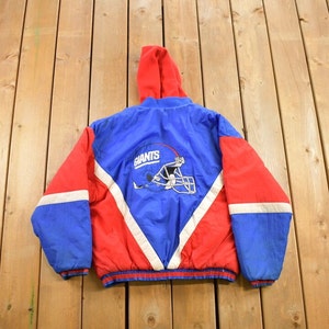 May include: A blue and red reversible jacket with a white stripe down the sleeves. The back of the jacket features a white and blue New York Giants logo with the word "Giants" above it.