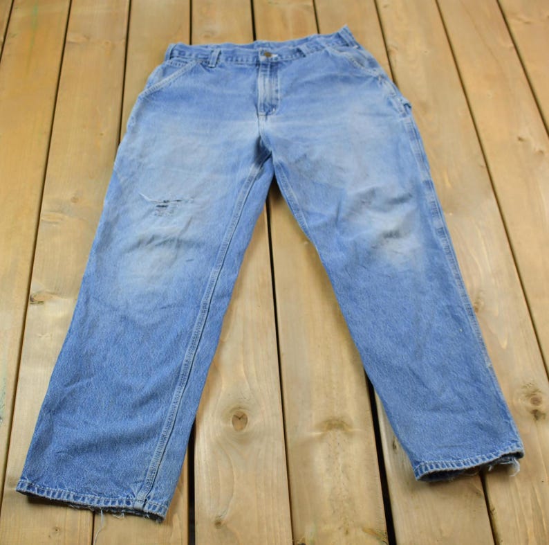 May include: A pair of light blue denim carpenter jeans with a worn look. The jeans have a straight leg and multiple pockets.