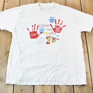 May include: White t-shirt with a red handprint and the text "Children Are Beautiful" and "Nobody Paints More Country".