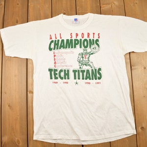 May include: White crew neck t-shirt with a green and red graphic. The graphic reads "ALL SPORTS CHAMPIONS TECH TITANS" with the years 1989-1991. A cartoon figure is also present in the graphic.