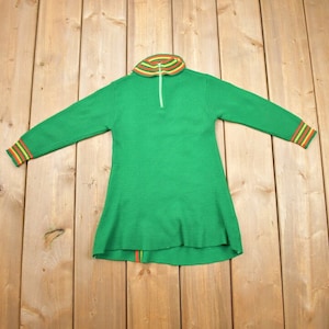 May include: A green long-sleeved sweater with a zip and a striped collar and cuffs. The sweater has a flared hem.