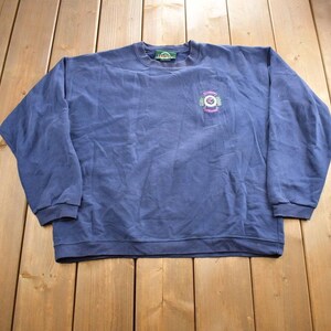 May include: A navy blue long-sleeved sweatshirt with a green logo and embroidered design on the front. The logo features a green circle with a white outline and the text "Green Mountain" inside. The embroidered design features a green, pink, and white design with the text "Green Mountain" and "The Original" inside.