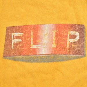 May include: A yellow t-shirt with a red, white, and gray "FLIP" logo printed on the front.