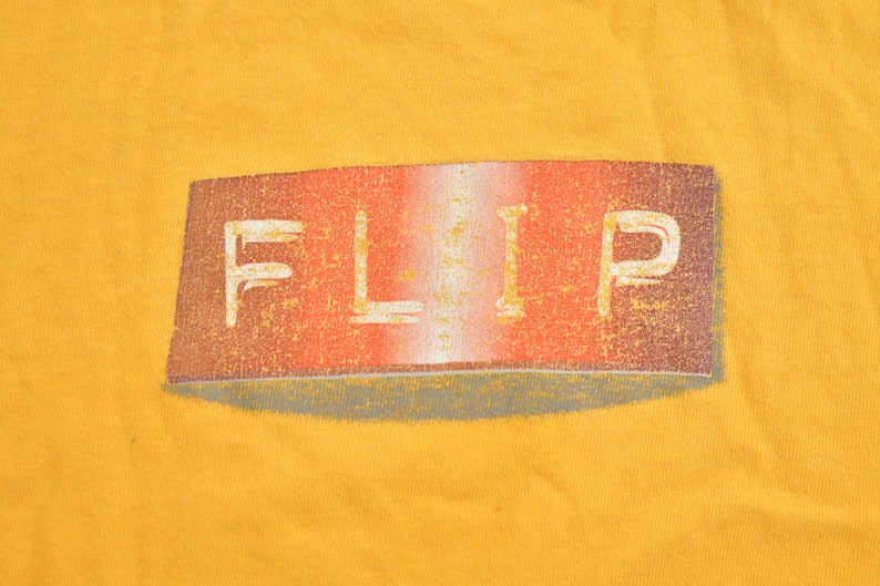 May include: A yellow t-shirt with a red, white, and gray "FLIP" logo printed on the front.