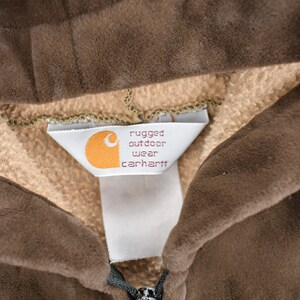 May include: Close-up of a brown Carhartt hoodie with a white tag that reads "rugged outdoor wear carhartt".