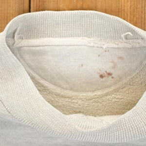 K&ouml;nnte beinhalten: Nahaufnahme der Innenseite eines hellgrauen Sweatshirtkragens. Der Kragen ist gerippt und hat eine weiche, flauschige Innenseite. Auf der Innenseite des Kragens befinden sich ein paar kleine, rotbraune Flecken.