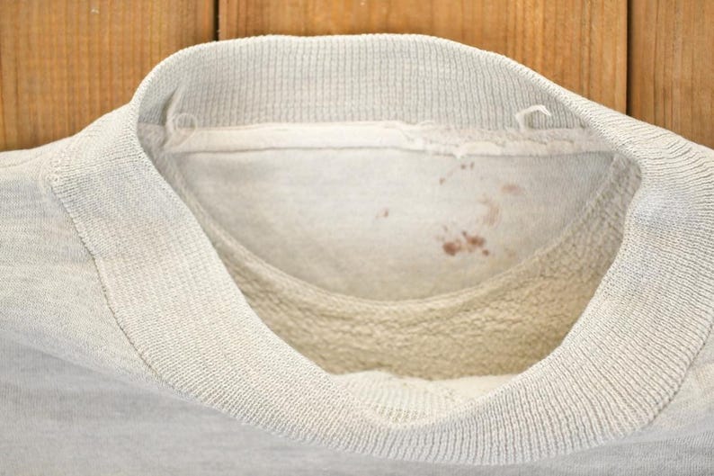 K&ouml;nnte beinhalten: Nahaufnahme der Innenseite eines hellgrauen Sweatshirtkragens. Der Kragen ist gerippt und hat eine weiche, flauschige Innenseite. Auf der Innenseite des Kragens befinden sich ein paar kleine, rotbraune Flecken.